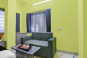 A room with a green wall, a window with curtains, a sofa, a small table with a tray, and a bed. - Hotel O Ecospace Business Park Kolkata (Kolkata)