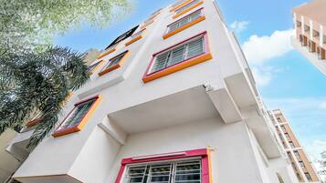 A multi-story building with a white facade, multiple windows with orange and pink frames, and a visible balcony.