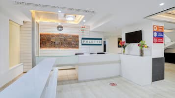 Zona de recepción con mostrador, un reloj y un letrero que indica medidas de distanciamiento social.