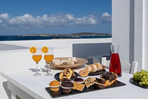 Una mesa con diversos pasteles, bebidas y una vista panorámica del mar.