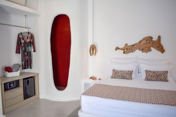 A bedroom with a bed, a red accent wall, a hanging light fixture, and a small bedside table. - Angels Pillow (Paros)