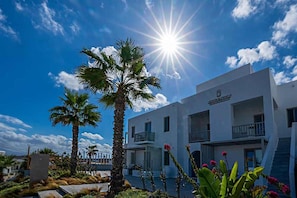 A hotel with a white facade, balconies, and palm trees in the foreground. - Angels Pillow (Paros)