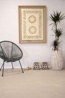 Una obra de arte enmarcada en una pared, una silla negra, un jarrón tejido grande con una planta, y dos cestas de piedra pequeñas.
