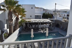 A pool area with lounge chairs and umbrellas, surrounded by white buildings and palm trees.