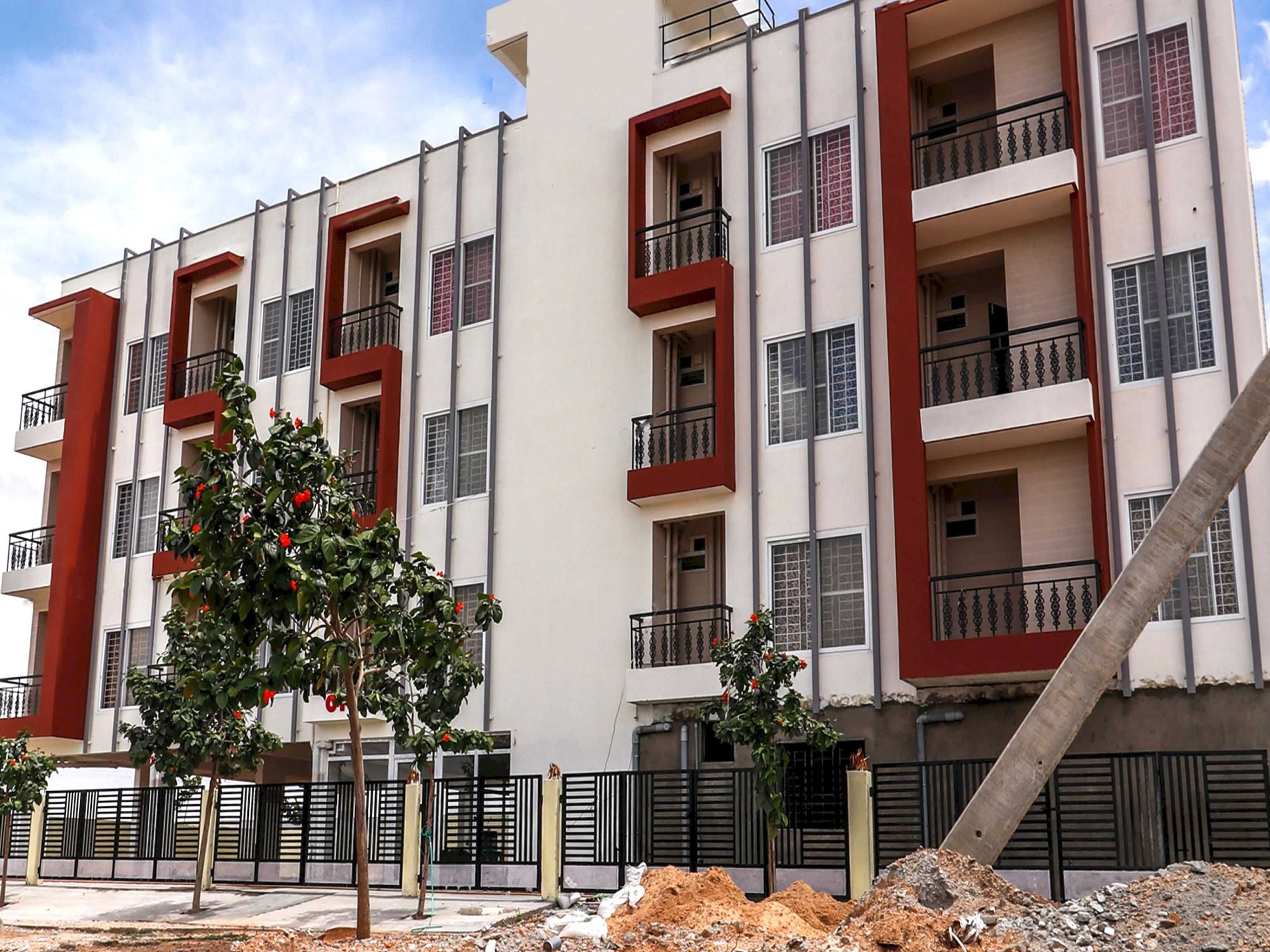 A multi-story residential building with balconies, a paved ground floor, and a construction site in the foreground.
