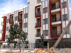 Un edifici d'apartaments de diversos pisos amb balcons, un soterrani pavimentat i una obra en primer pla.