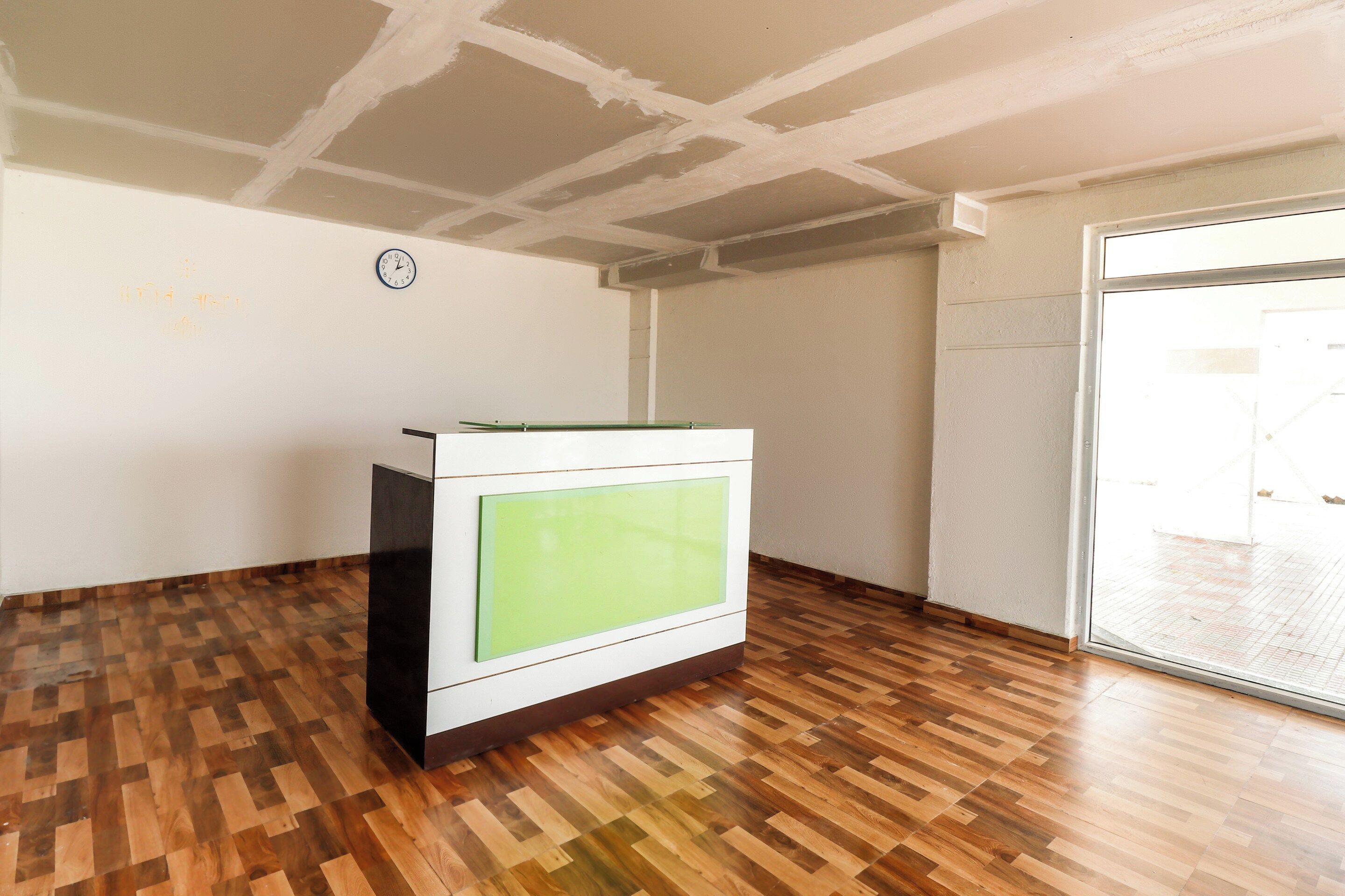 A room with a wooden parquet floor, a white cabinet with a green panel, and a clock on the wall.