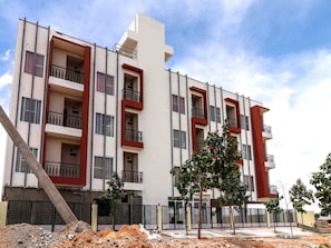 A multi-story residential building with balconies, a gated entrance, and a construction site in the foreground. - Collection O Dew Drops (Anantapur)