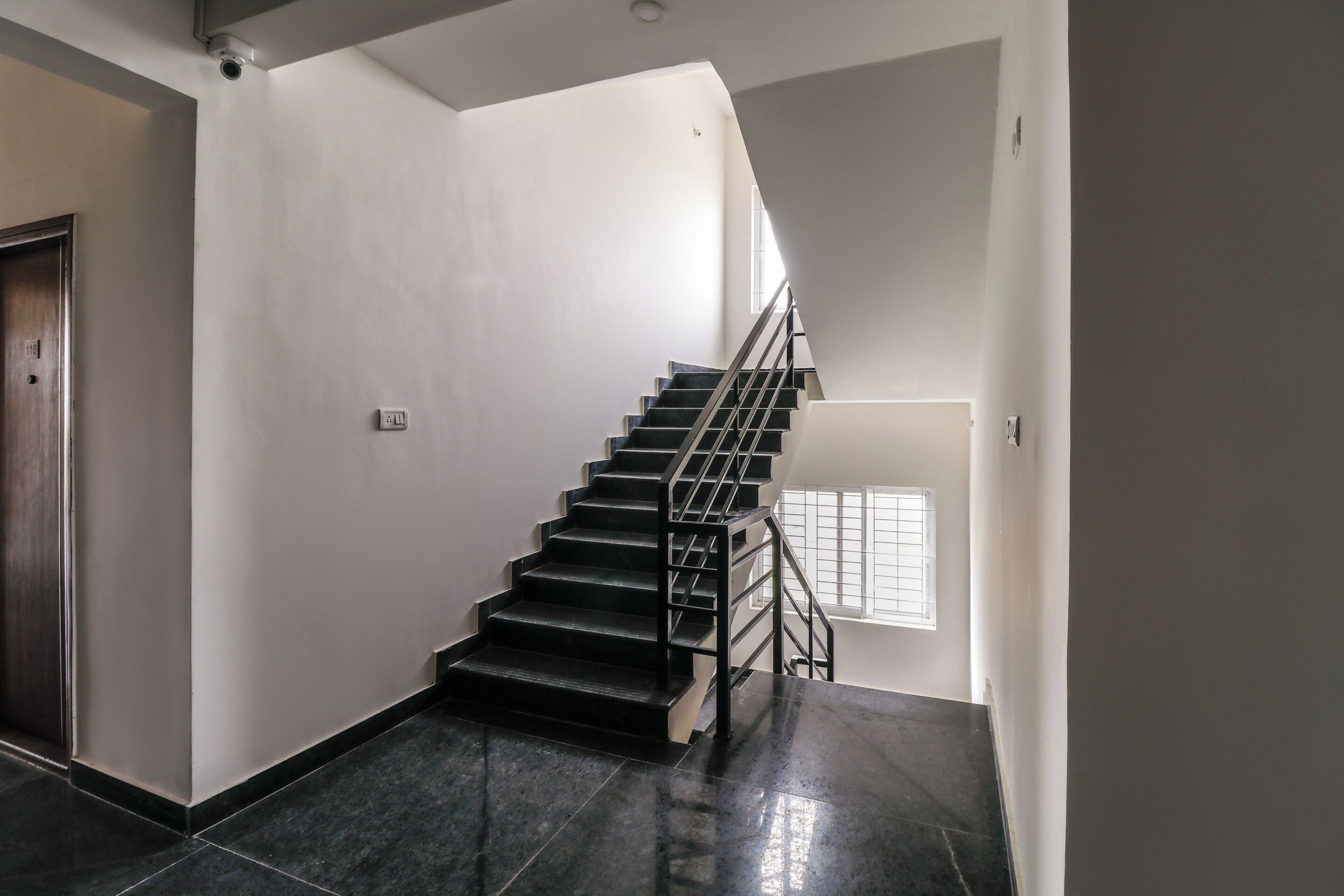 Un escalier avec une rampe métallique menant à un palier doté d’une fenêtre.
