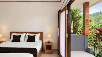 Habitación de hotel con una cama grande, una mesita de noche, una lámpara y un ventanal corredero que da a un balcón con plantas.