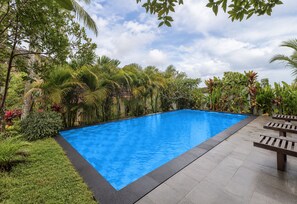 A rectangular swimming pool with clear blue water, surrounded by lush greenery and a cloudy sky. - Belvilla Bhavana Cottage (Penida Island)