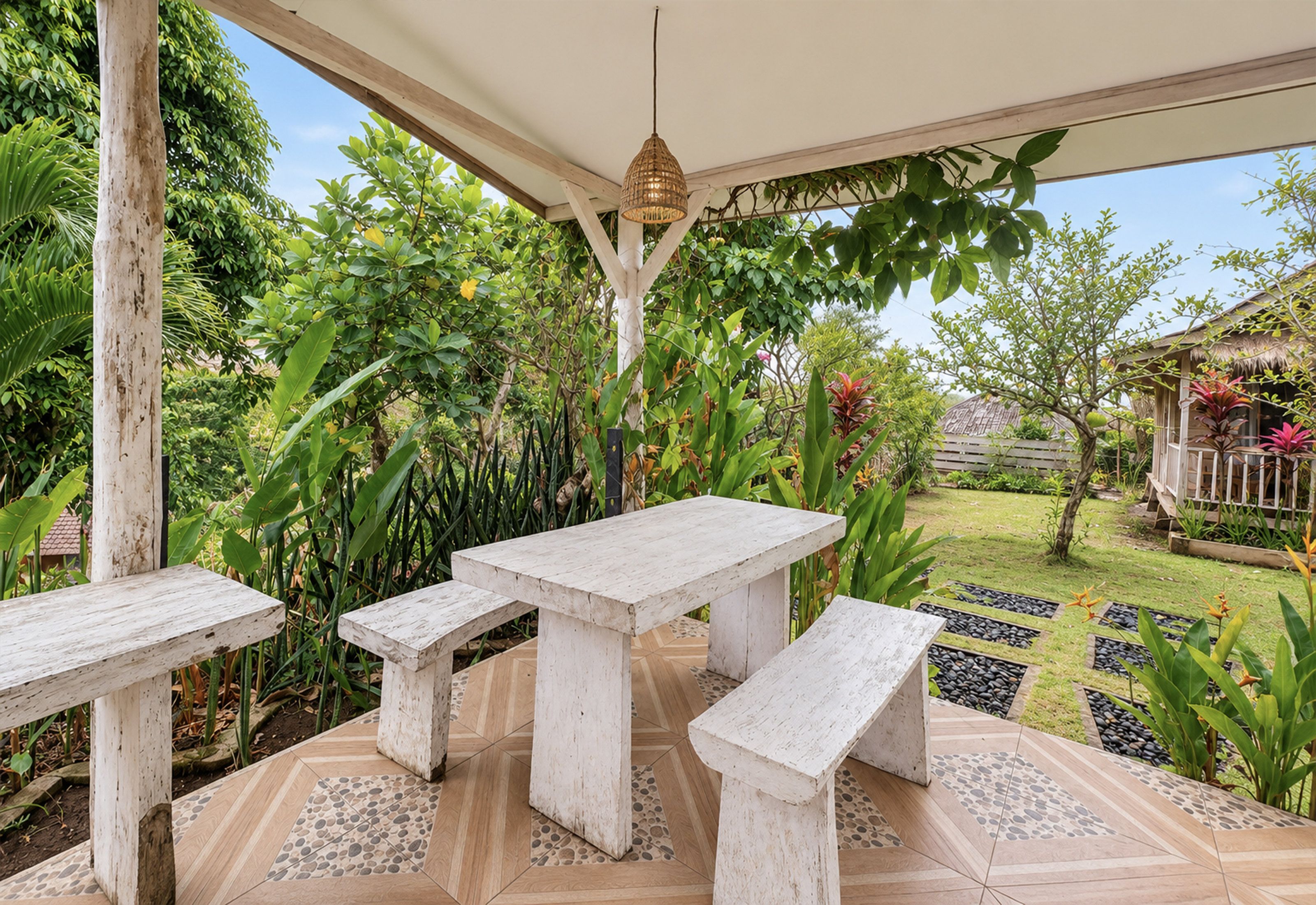 Une terrasse extérieure avec une table et des bancs en bois, entourée d’une végétation luxuriante et dotée d’un sol carrelé à motifs.