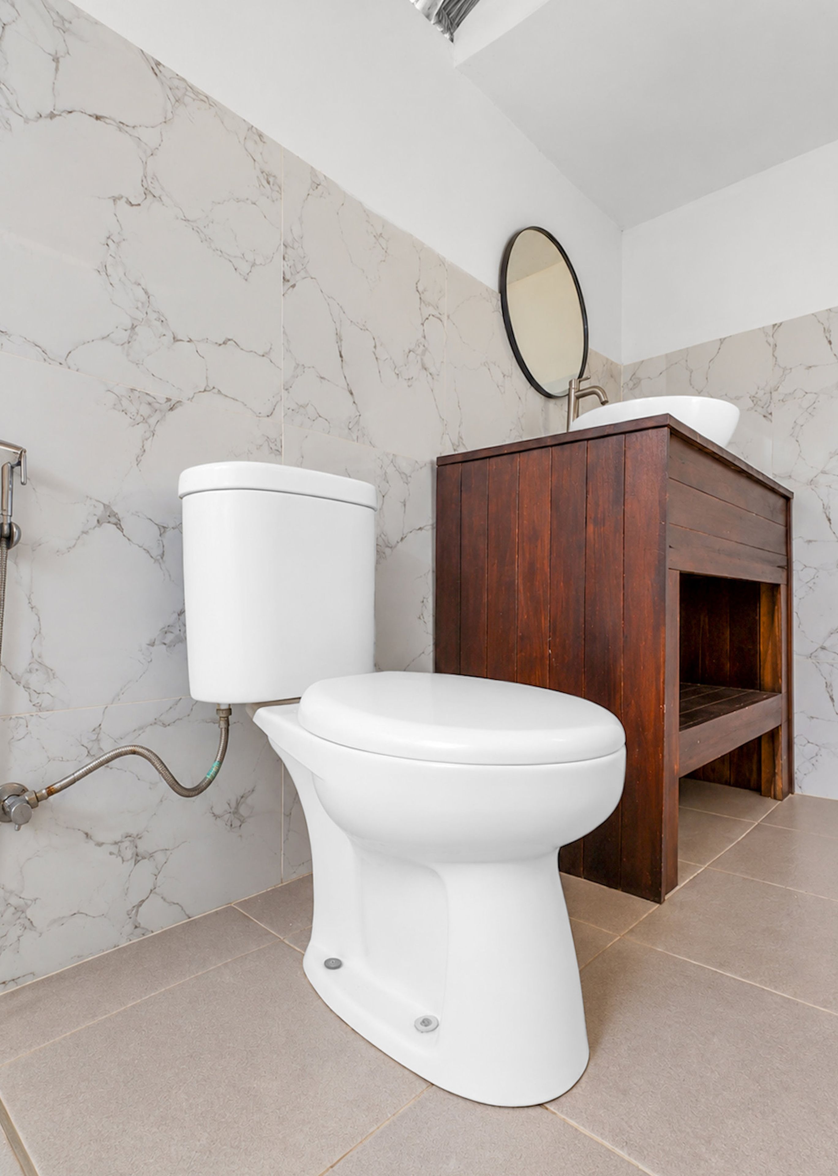 Un baño con inodoro, tocador de madera, paredes de mármol y un espejo.
