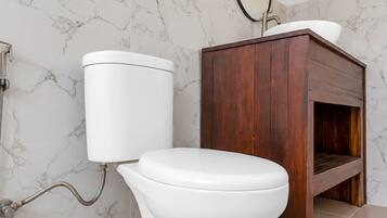Un baño con inodoro, tocador de madera, paredes de mármol y un espejo.