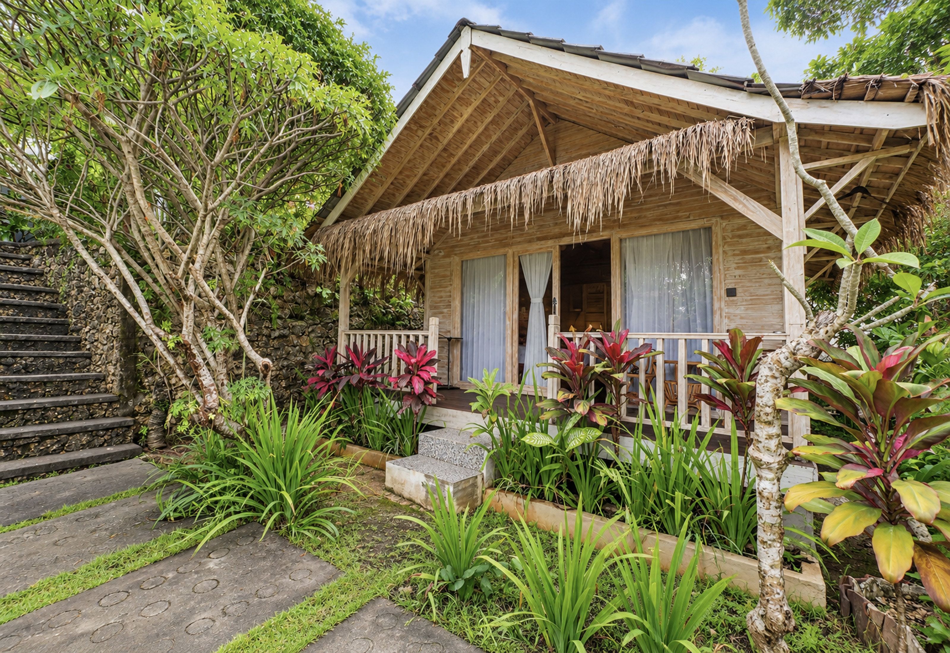 Una casa de madera con techo de paja, rodeada de exuberante follaje y plantas tropicales.