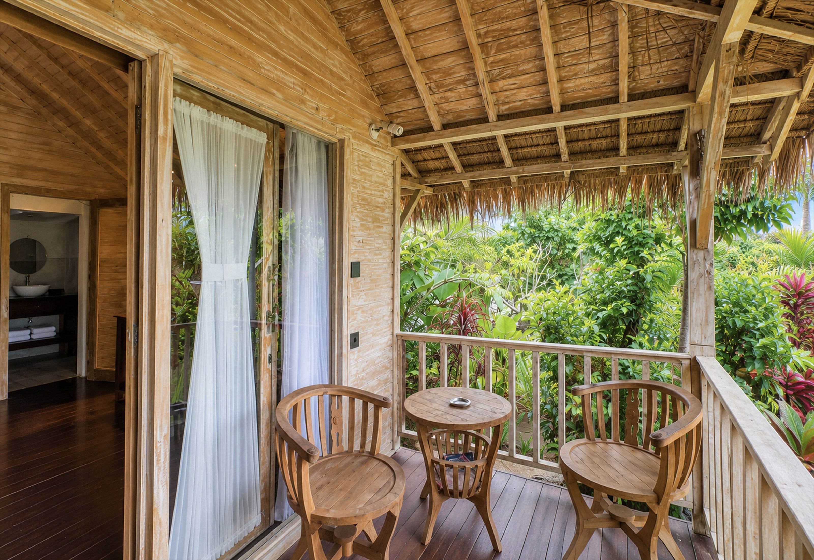 A wooden balcony with two wooden chairs and a small table, overlooking a lush garden.