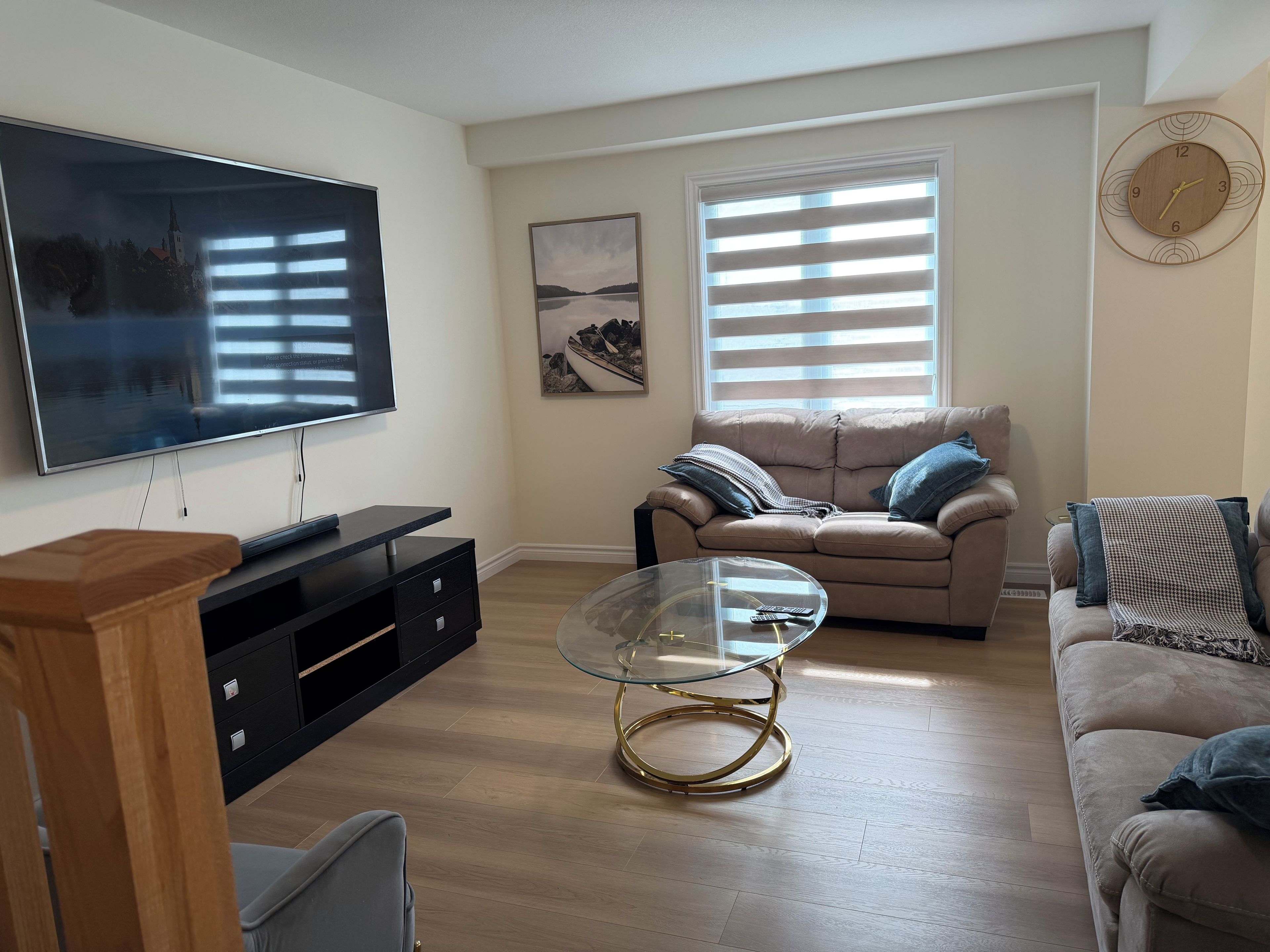 Un salon avec un téléviseur à écran plat, une table basse en verre, un canapé beige et une table d’appoint en bois.