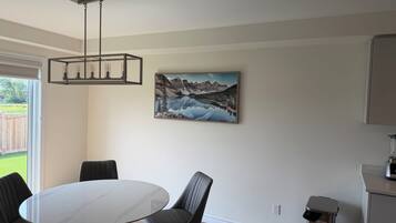 Un'area pranzo con un tavolo rotondo e sedie, un quadro appeso al muro e un cestino.