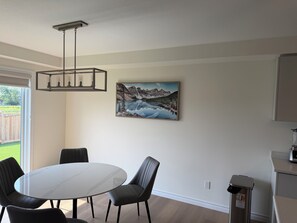 Ein Essbereich mit einem runden Tisch, Stühlen, einem Bild an der Wand und einem Mülleimer.