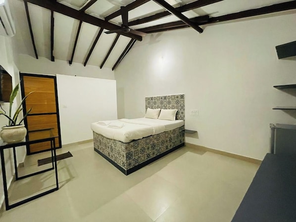 A bedroom with a bed, a nightstand, a potted plant, and a wooden door.