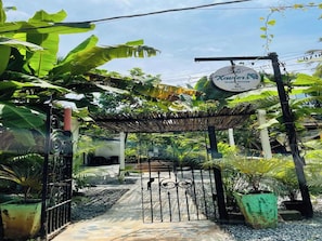 A gated entrance with a sign for 'Xavier House Guest House Bar & Restaurant' and a tropical garden setting.