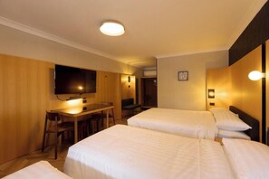 Una habitación de hotel con dos camas, un escritorio con sillas, un televisor y una lámpara fijada a la pared.