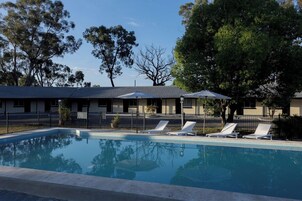 Una piscina con sillones de descanso, un área cercada y un edificio con techo de tejas.