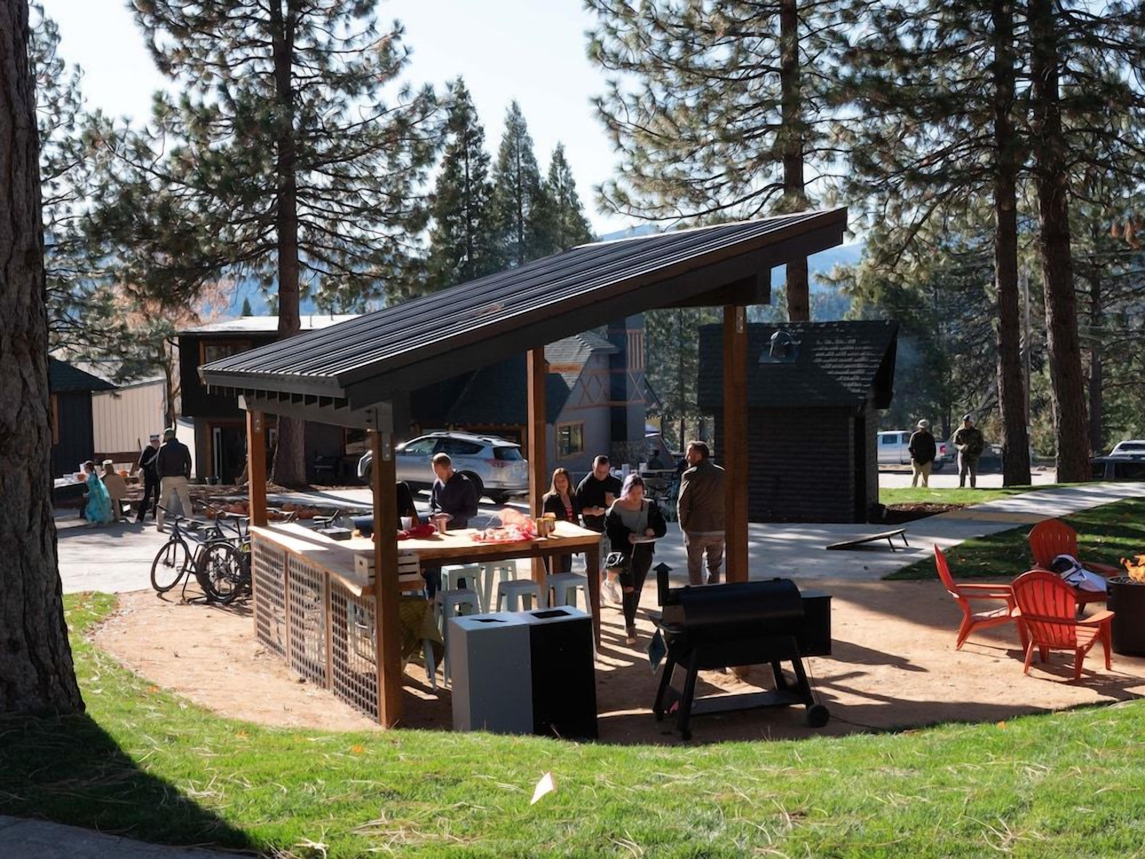 An outdoor seating area with a covered structure, a barbecue grill, and a wooden table.