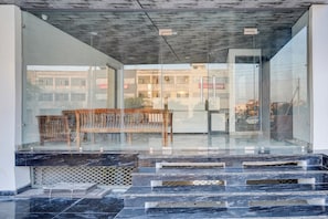 Un edificio moderno con fachada de vidrio, un banco de madera y una escalera que lleva a una entrada.