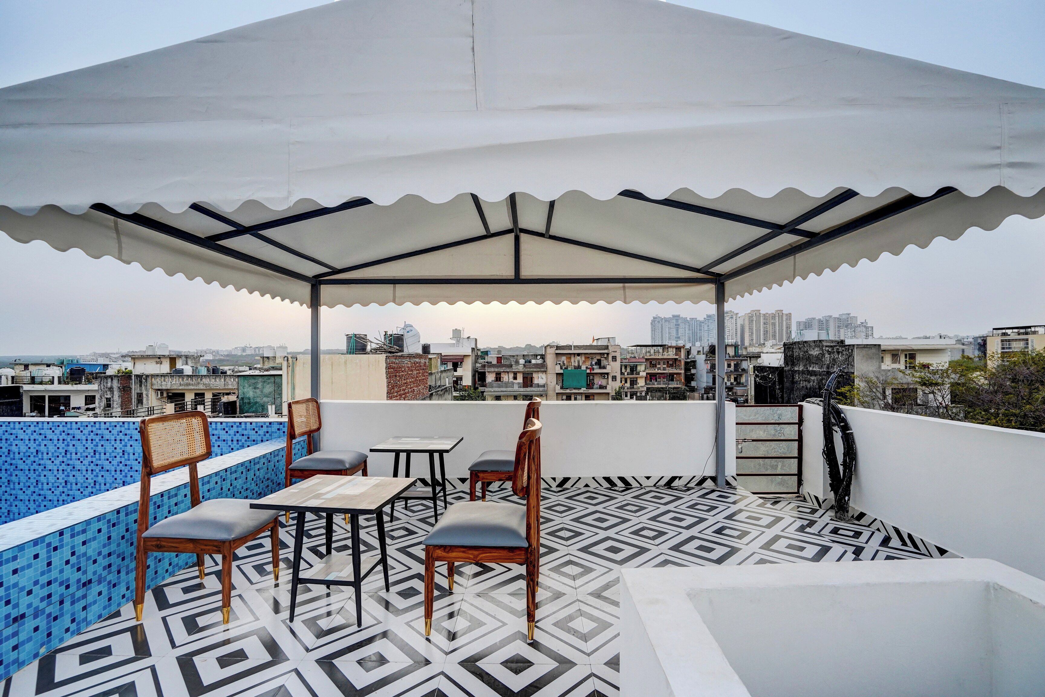 Une terrasse sur le toit avec un sol à motifs, un espace salon couvert avec des chaises et des tables, et une vue sur le paysage urbain en arrière-plan.