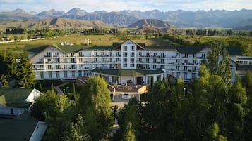 Un grand hôtel à plusieurs étages, doté d’une façade symétrique, d’une cour intérieure et offrant une vue sur les montagnes en arrière-plan.