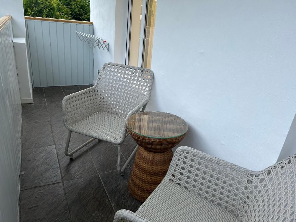 A balcony with two wicker chairs and a round table, a white wall, and a grey tiled floor.