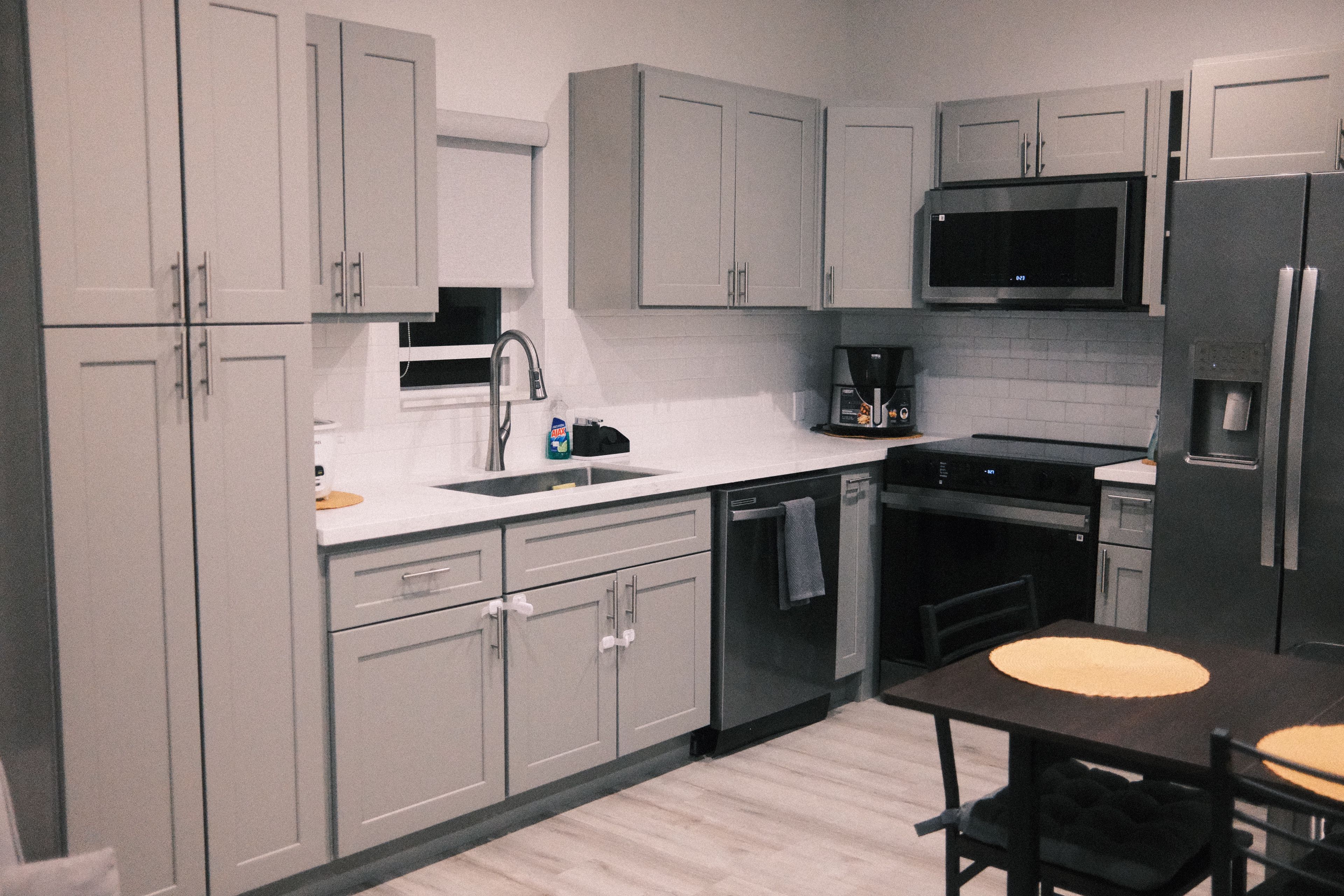 A modern kitchen with grey cabinets, a stainless steel sink, a microwave, and a refrigerator.