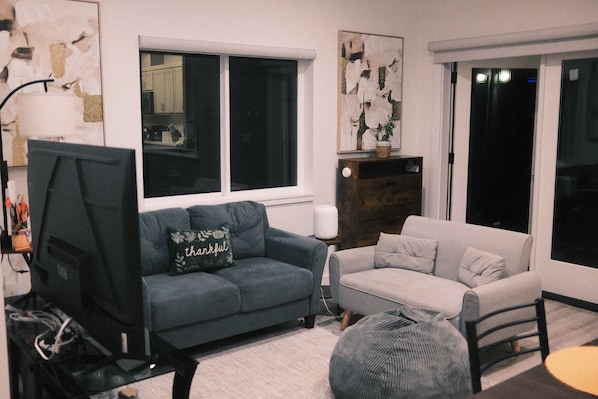 A living room with a dark blue sofa, a light grey sofa, a television, and a large window.