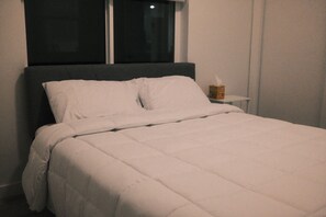 Un llit amb roba de llit blanca, una tauleta de nit amb una caixa de mocadors i una finestra amb vista al cel nocturn.