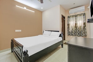 Een slaapkamer met een bed, een bureau, een airconditioner en een raam met gordijnen.