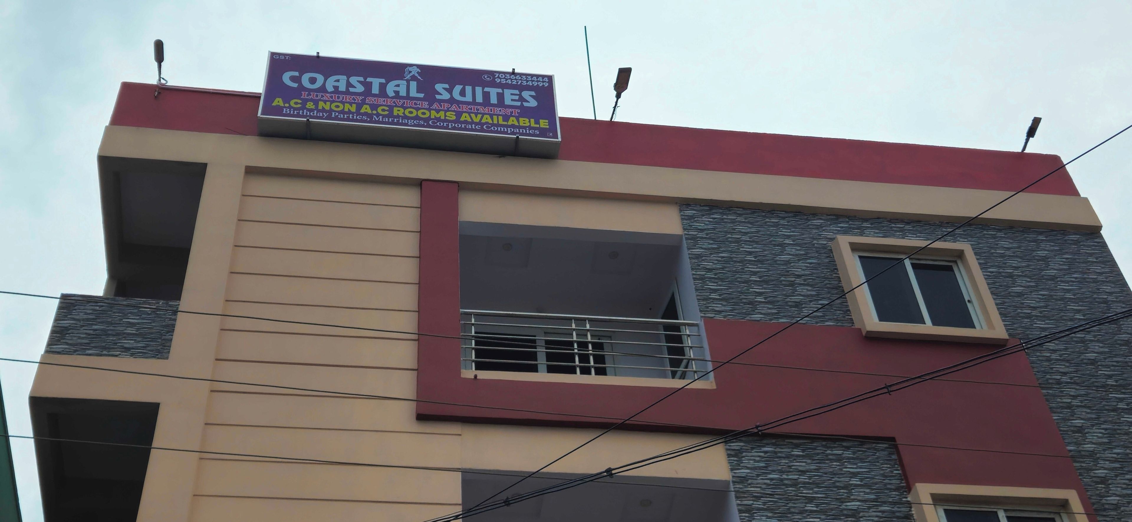 Ein mehrstöckiges Gebäude mit einem Schild, das Coastal Suites wirbt und daraufhinweist, dass klimatisierte und nicht-klimatisierte Zimmer verfügbar sind.