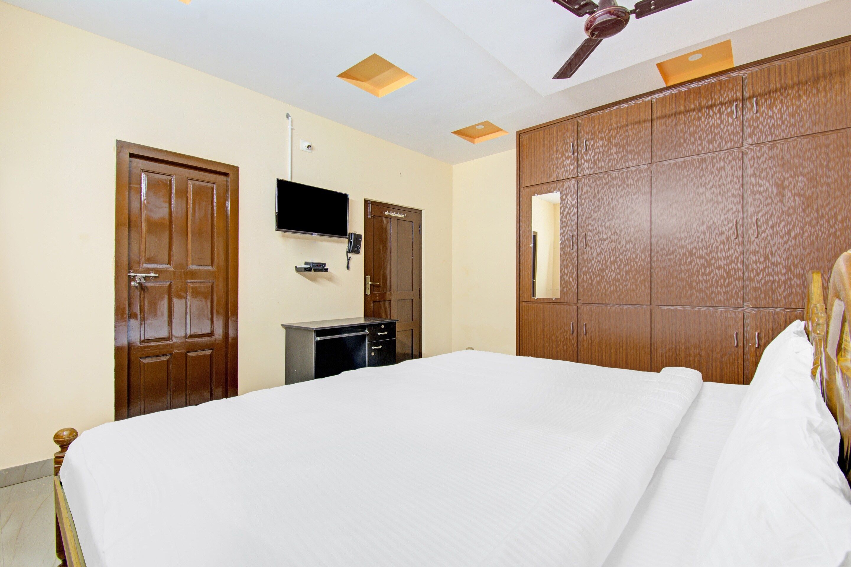 Ein Hotelzimmer mit Bett, Schreibtisch, Wandfernseher und Deckenventilator.