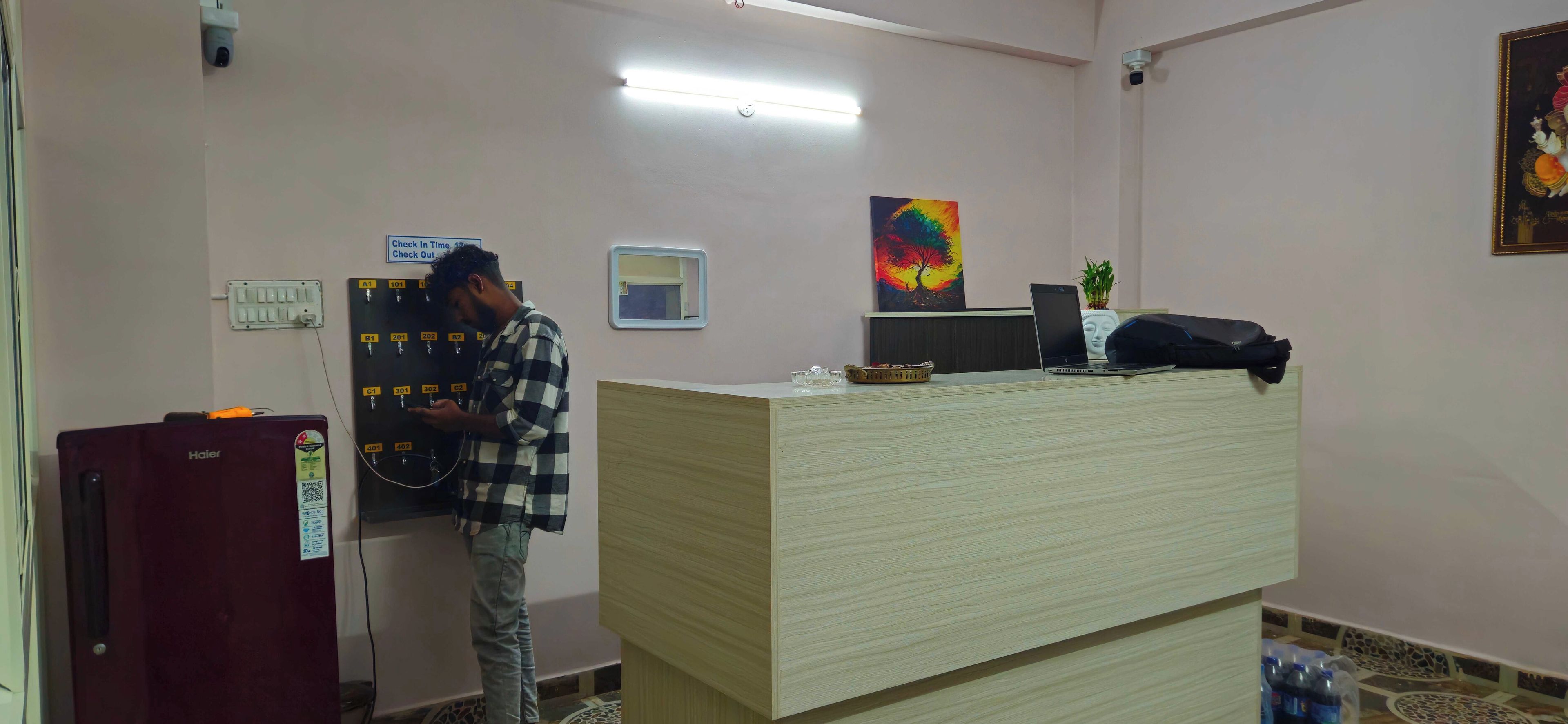 Un espace d’accueil comprenant un comptoir d’enregistrement, un ordinateur et un réfrigérateur de la marque Haier.