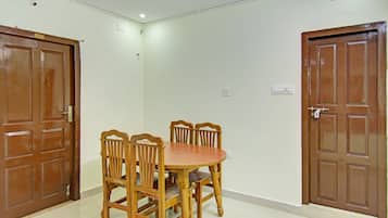Une pièce avec une table et des chaises de salle à manger en bois, deux portes en bois et un interrupteur sur le mur.