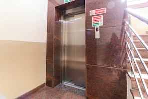 Un ascensor con un cartel de 'No Fumar' y una señal de seguridad contra incendios que indica usar las escaleras en caso de emergencia.