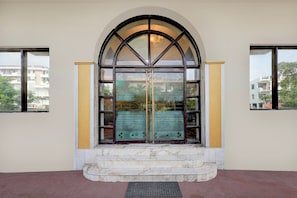 A building entrance with a large arched doorway, a set of steps leading up to it, and a small outdoor area with a metal grate. - Hotel O Taj Empire (Agra)