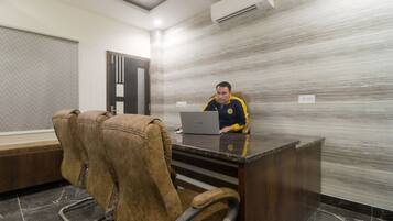 A man seated at a desk with a laptop in a room with a marble wall and a door with a window.