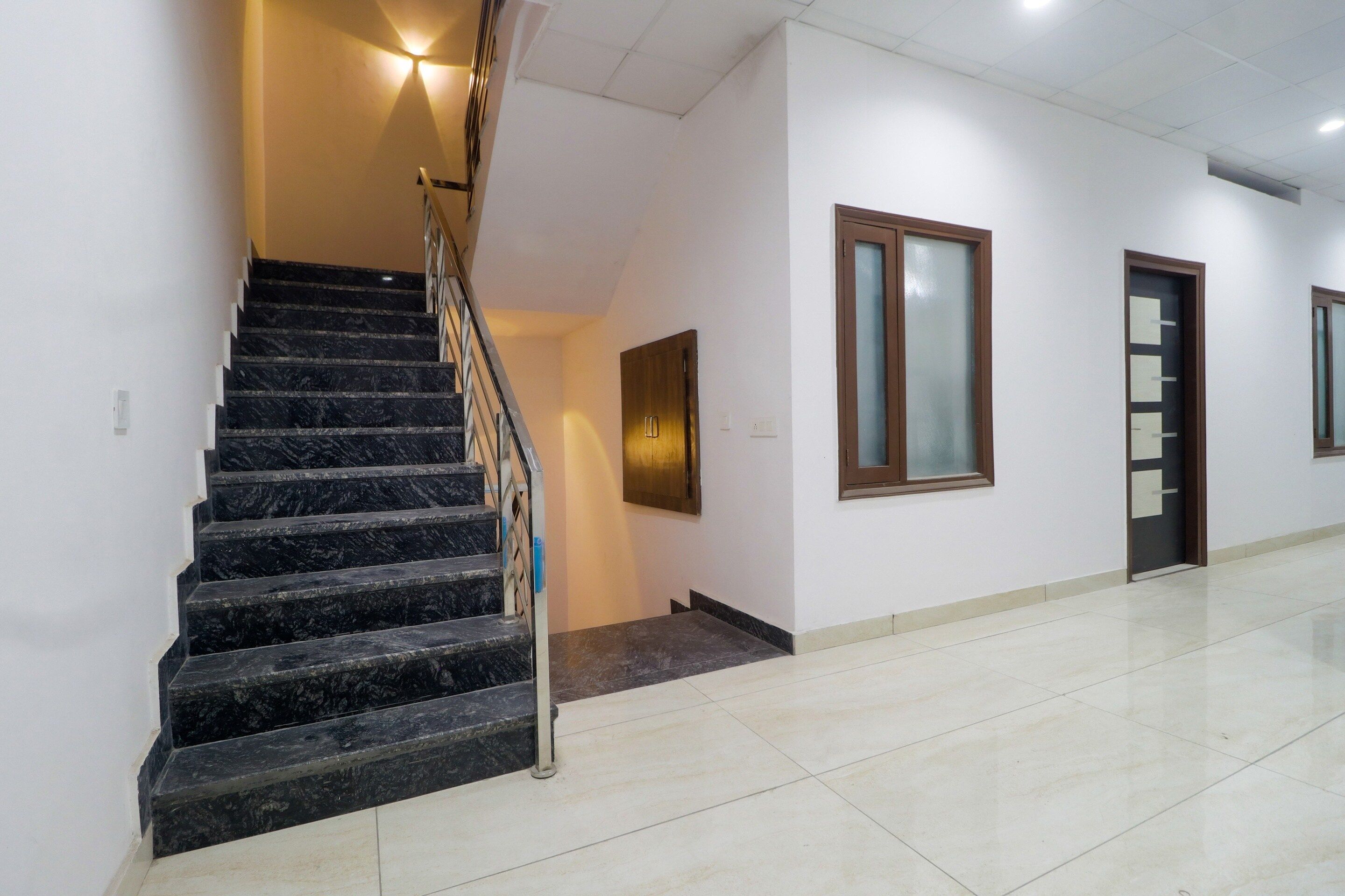 A staircase with a handrail leading to a landing, a door with a frosted glass panel, and a wall-mounted light fixture.