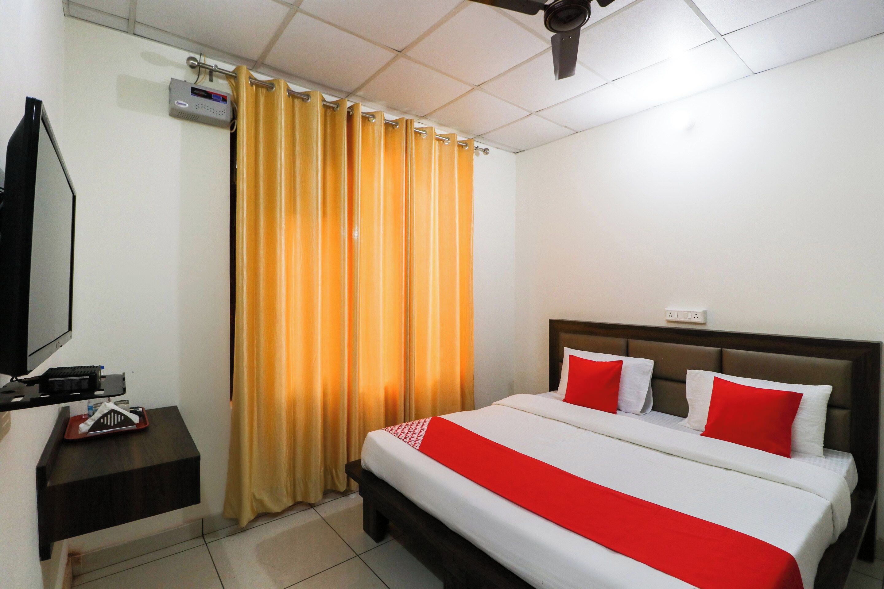 A hotel room with a bed, a TV, a desk, and a window with curtains.