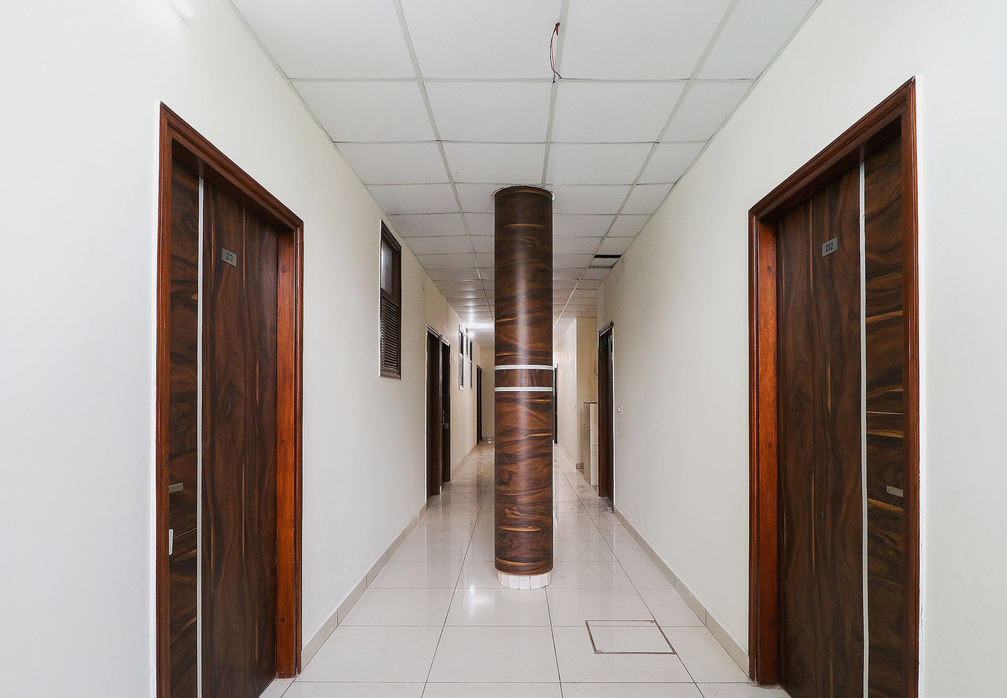 Un pasillo con puertas de madera a ambos lados, un pilar central y piso de baldosas.