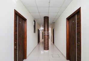 A hallway with wooden doors on either side, a central pillar, and a tiled floor. - Hotel O Rk Inn (Ludhiana)