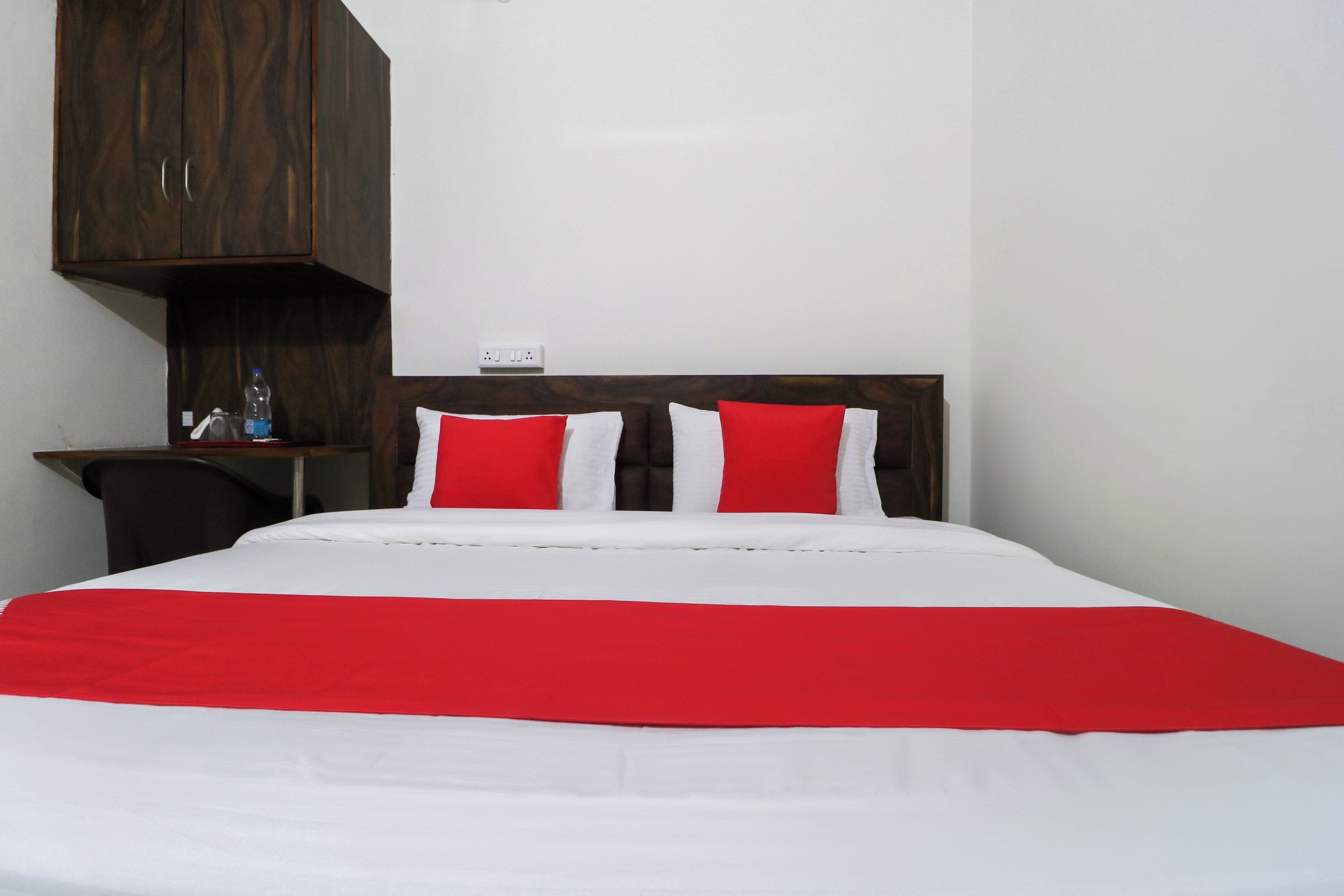 Una cama con ropa de cama blanca y roja, un cabecero de madera, un escritorio con una silla y una botella.