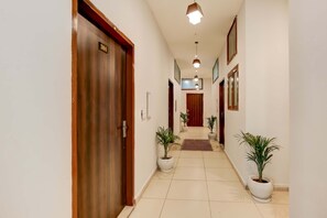 Un pasillo de hotel con una puerta de madera que dice '201', plantas en macetas y piso de baldosas.