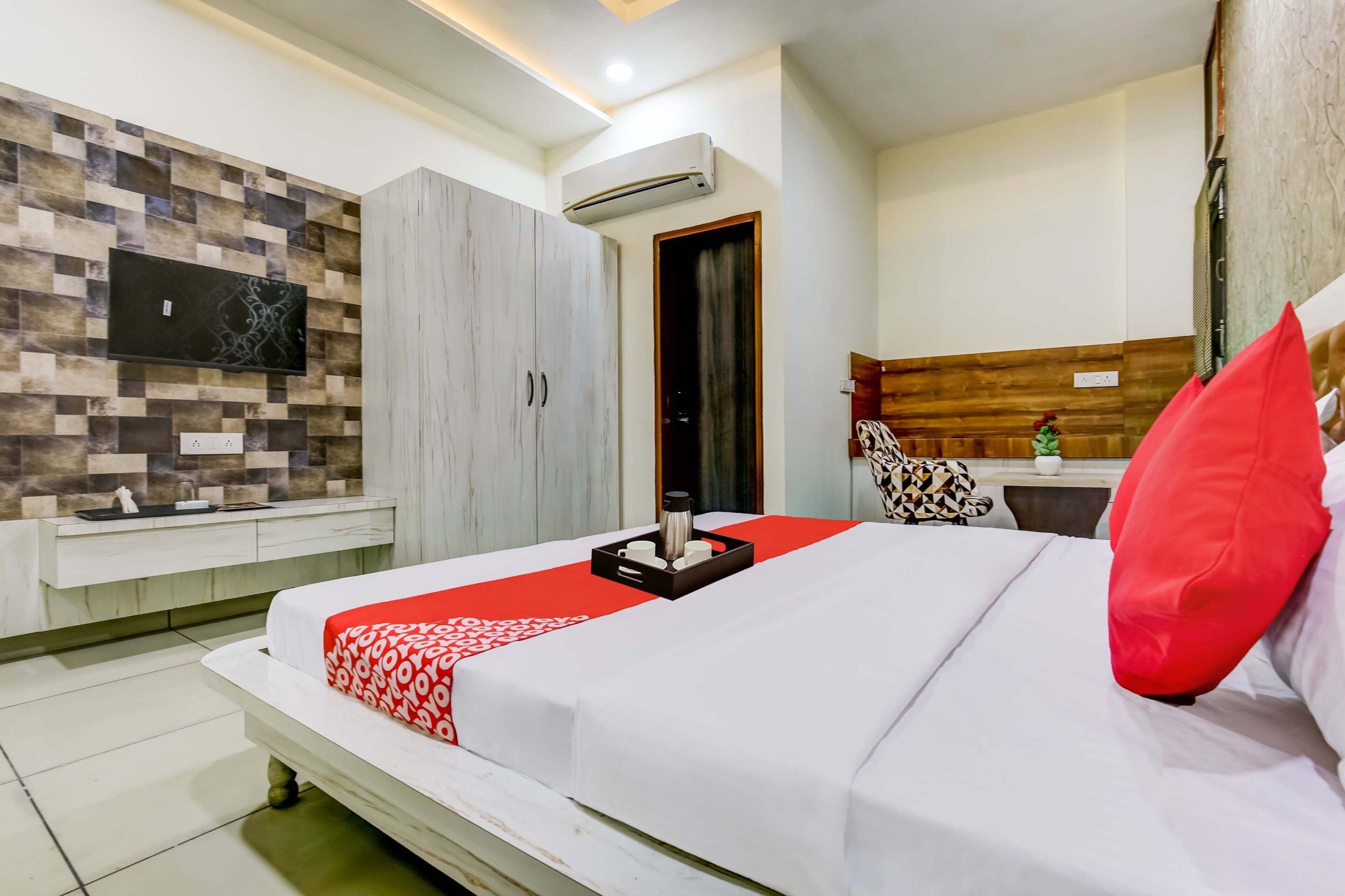 A hotel room with a bed, a TV mounted on the wall, a wardrobe, and a small kitchenette area.